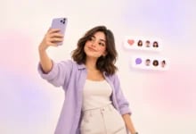 Pastel pembe-mor arka planda akıllı telefonla selfie çeken genç kadın ve yanında sosyal medya etkileşim balonları.